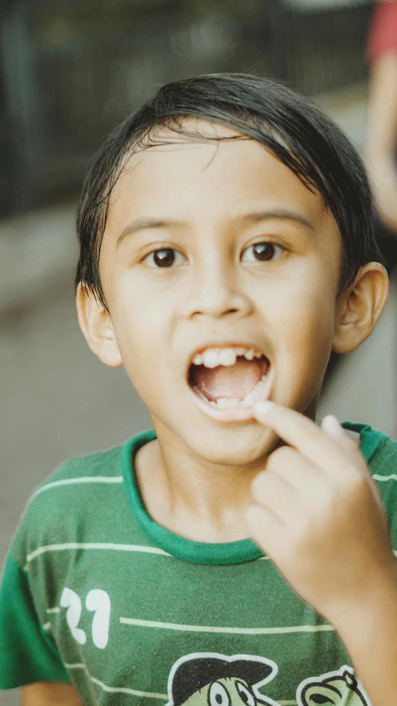 A young boy points at the gap where a milk tooth came out